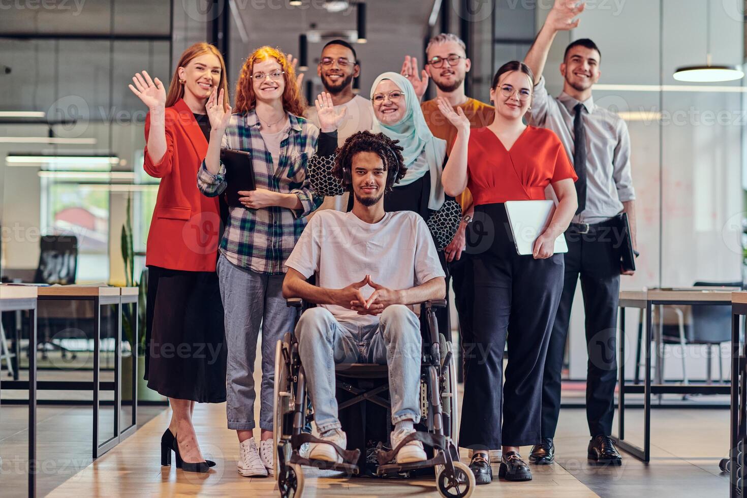 A diverse group of young business people congregates within a modern startup's glass-enclosed office, featuring inclusivity with a person in a wheelchair, an African American young man , and a hijab photo