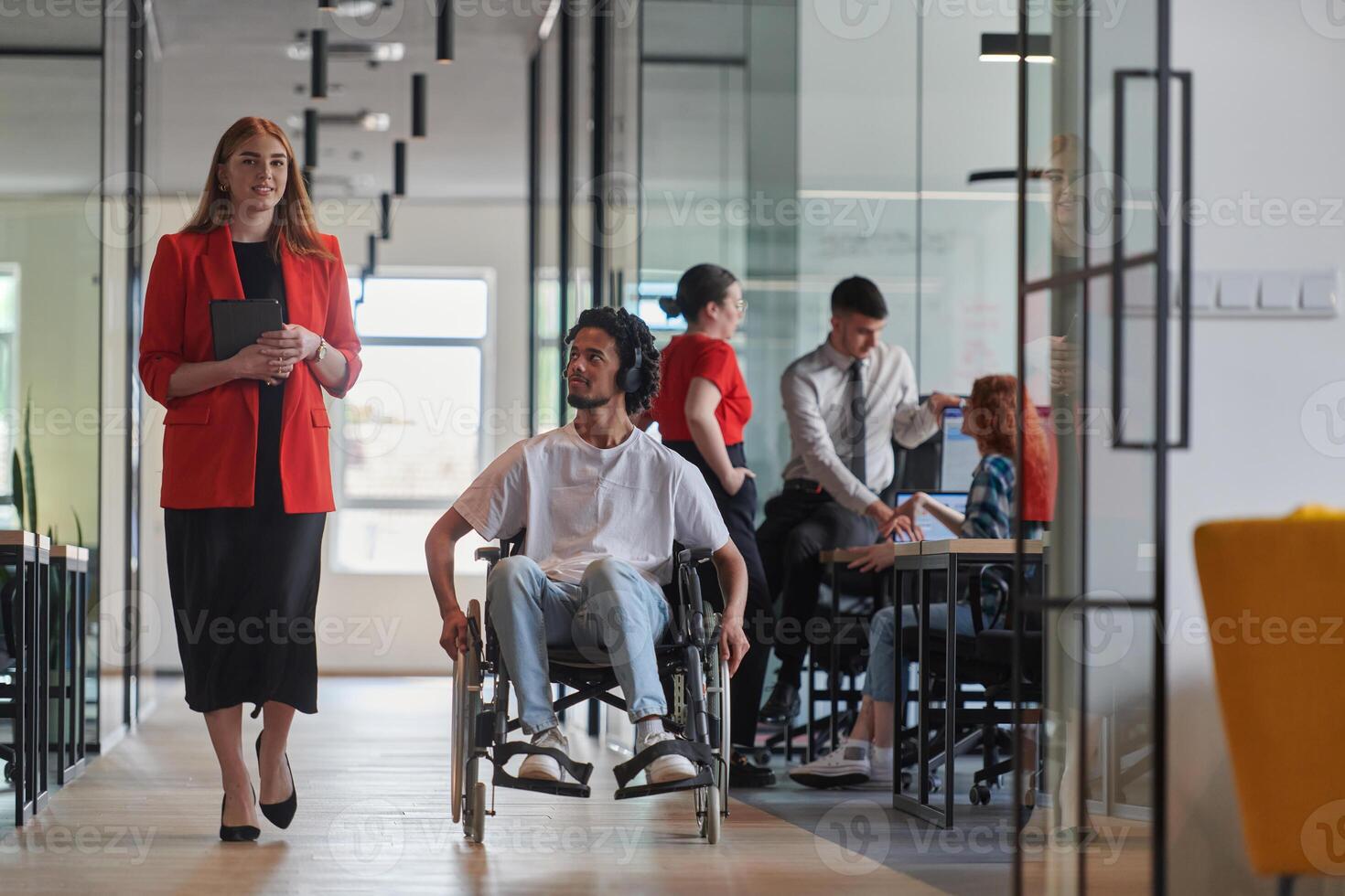 A group of young business people in a modern glass-walled office captures the essence of diversity and collaboration, while two colleagues, including an African American businessman in a wheelchair photo