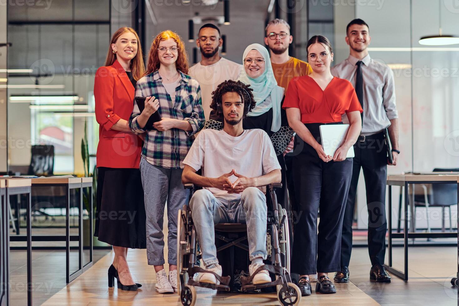 A diverse group of young business people congregates within a modern startup's glass-enclosed office, featuring inclusivity with a person in a wheelchair, an African American young man , and a hijab photo