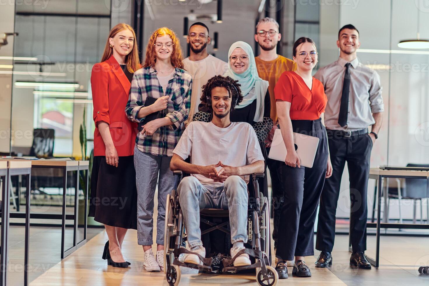 A diverse group of young business people congregates within a modern startup's glass-enclosed office, featuring inclusivity with a person in a wheelchair, an African American young man , and a hijab photo