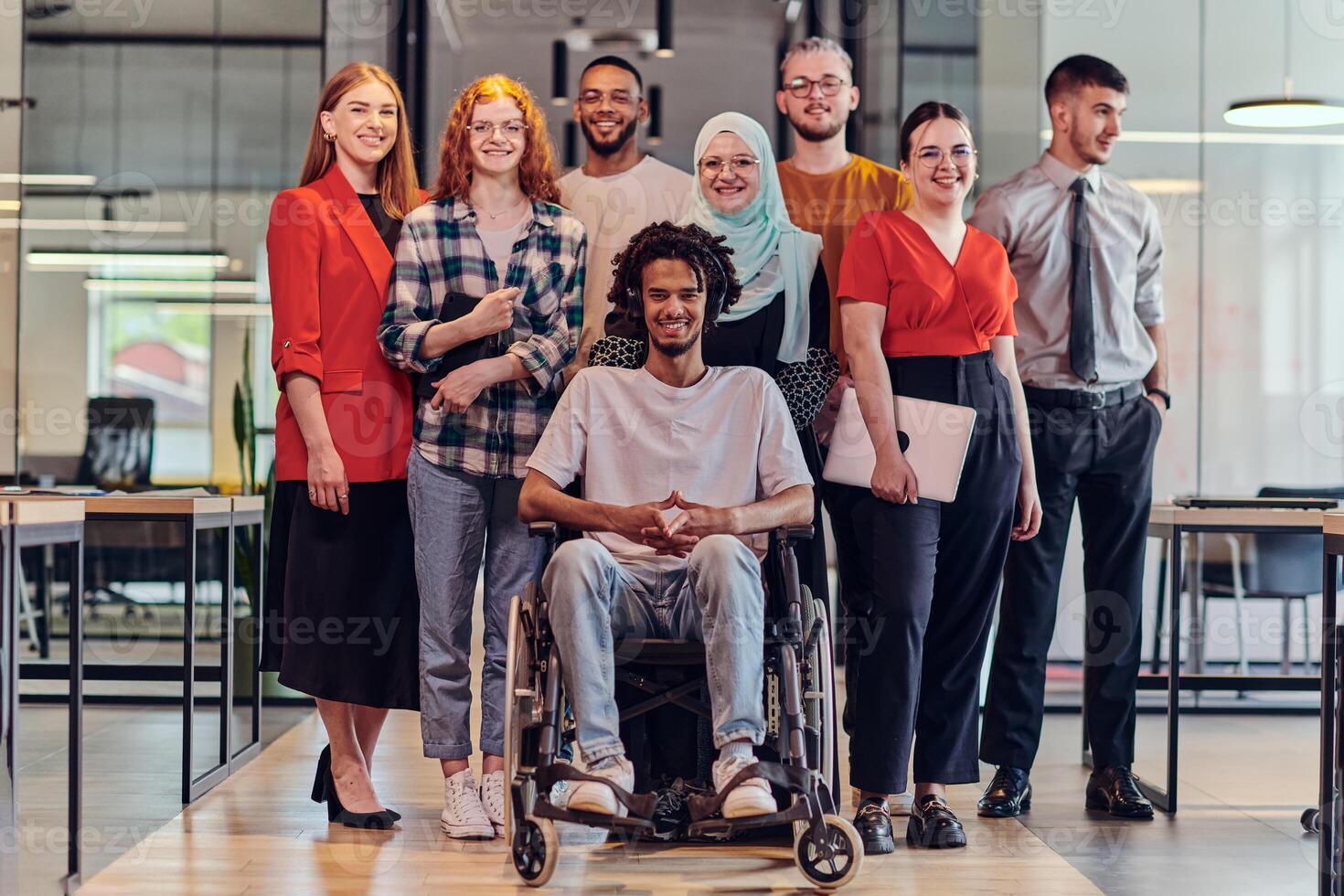 A diverse group of young business people congregates within a modern startup's glass-enclosed office, featuring inclusivity with a person in a wheelchair, an African American young man , and a hijab photo
