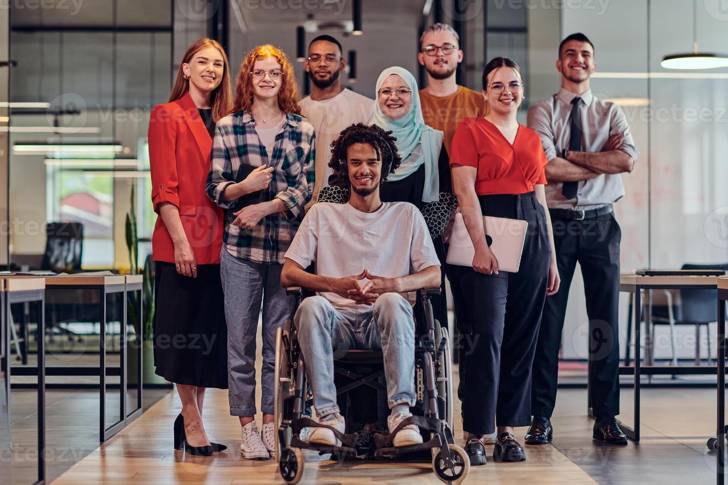 A diverse group of young business people congregates within a modern startup's glass-enclosed office, featuring inclusivity with a person in a wheelchair, an African American young man , and a hijab photo
