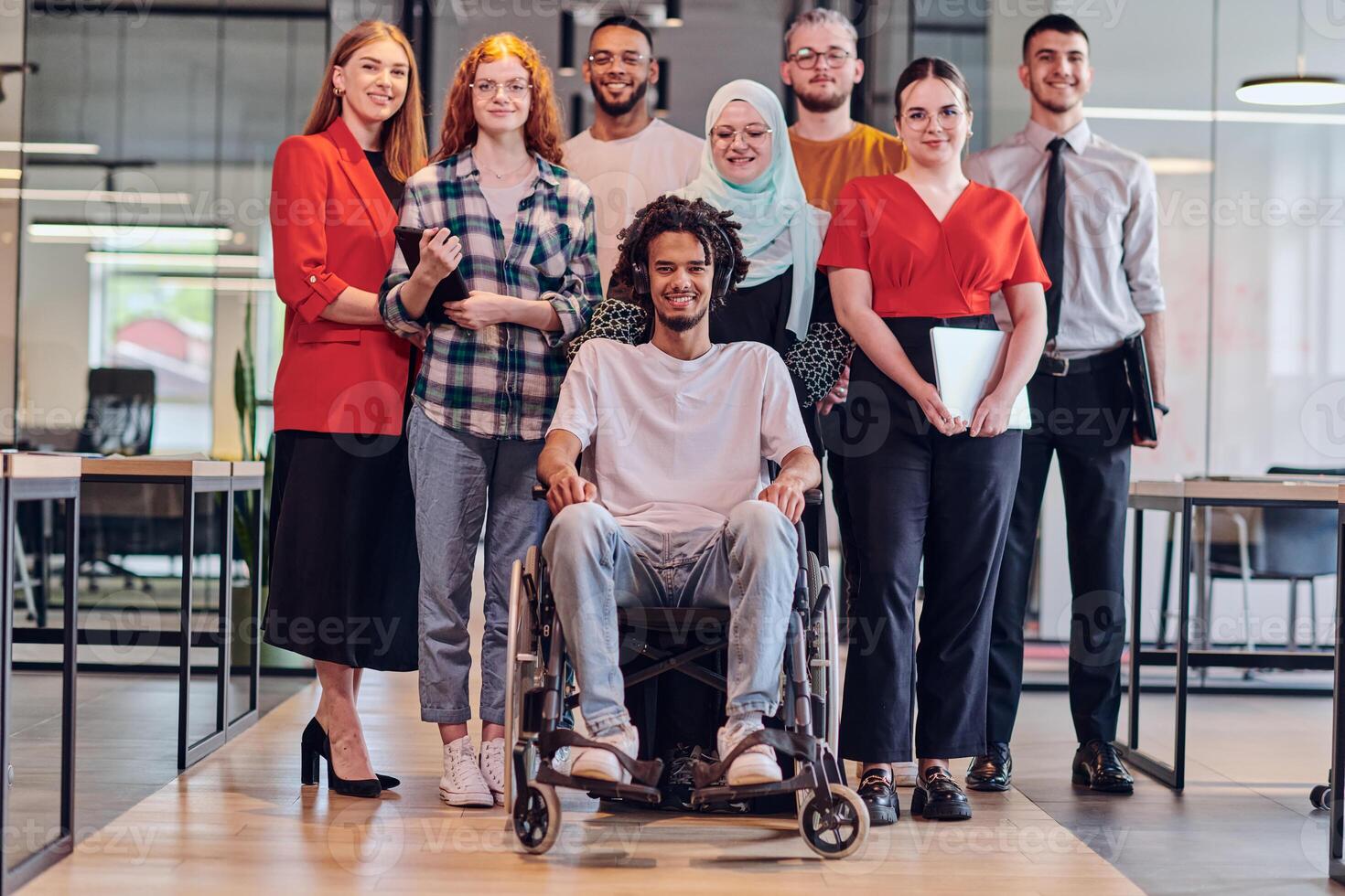 A diverse group of young business people congregates within a modern startup's glass-enclosed office, featuring inclusivity with a person in a wheelchair, an African American young man , and a hijab photo