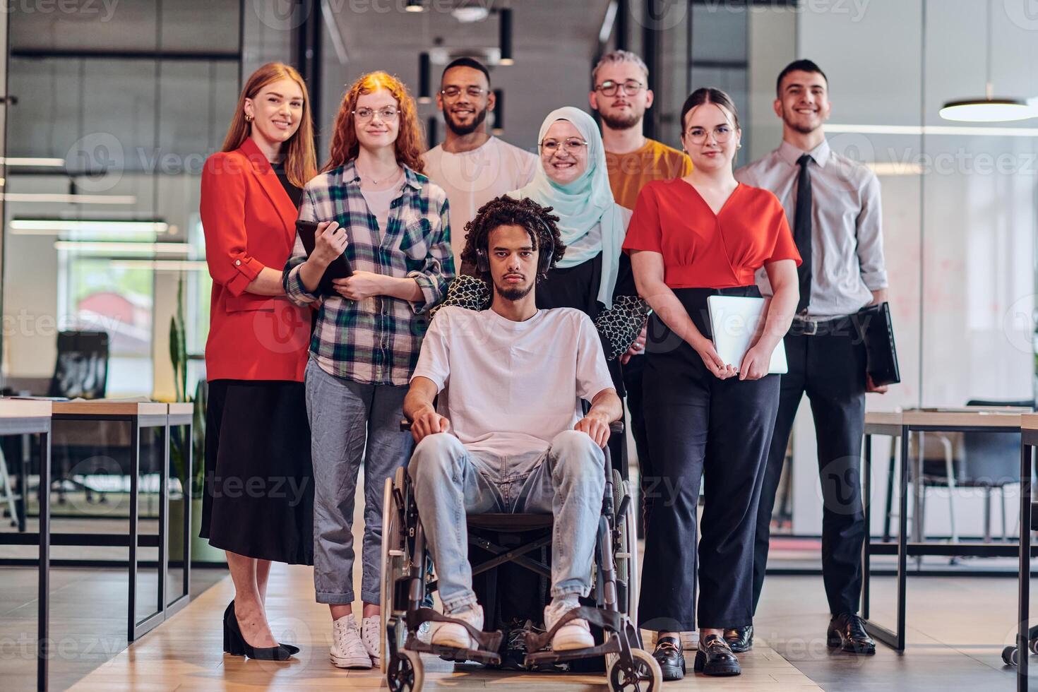 A diverse group of young business people congregates within a modern startup's glass-enclosed office, featuring inclusivity with a person in a wheelchair, an African American young man , and a hijab photo