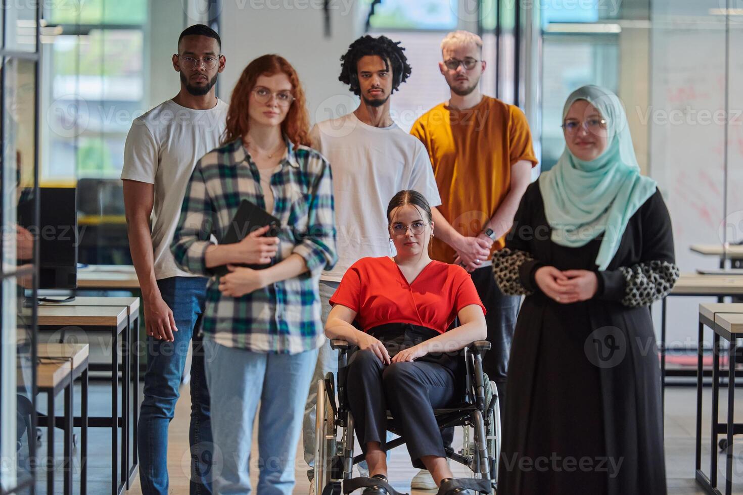 A diverse group of young business people congregates within a modern startup's glass-enclosed office, featuring inclusivity with a person in a wheelchair, an African American young man , and a hijab photo