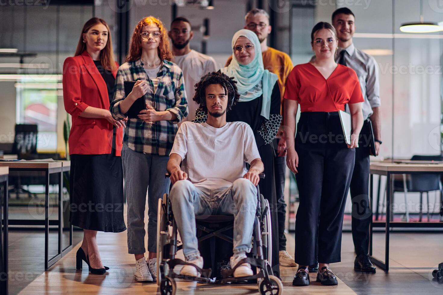 A diverse group of young business people congregates within a modern startup's glass-enclosed office, featuring inclusivity with a person in a wheelchair, an African American young man , and a hijab photo