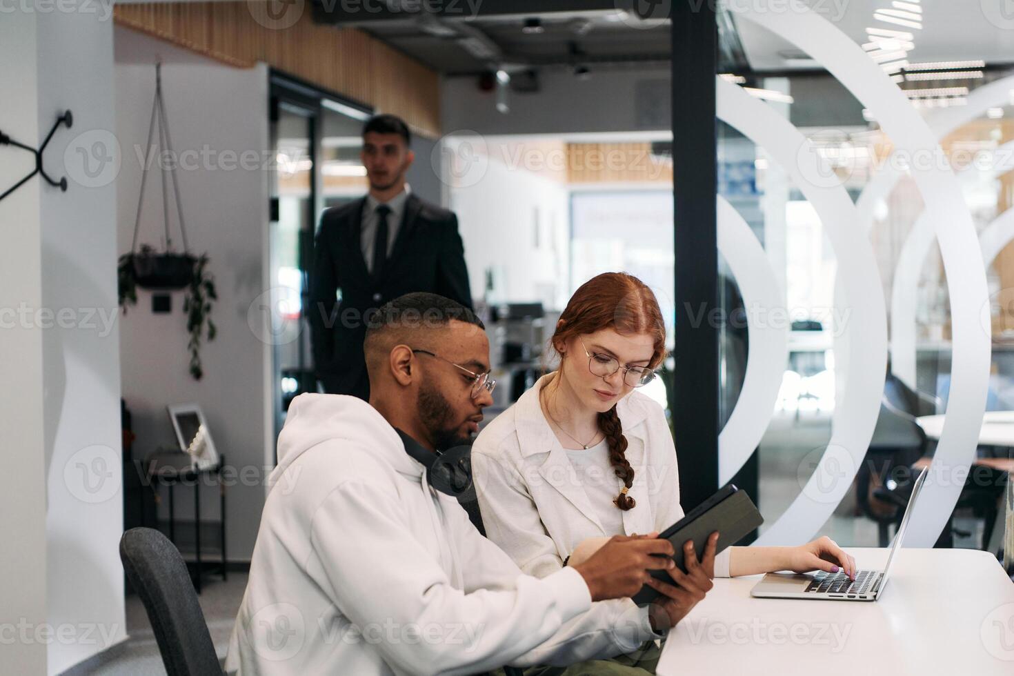 Two colleagues collaborating in a modern office while discussing a project using a tablet and laptop. photo