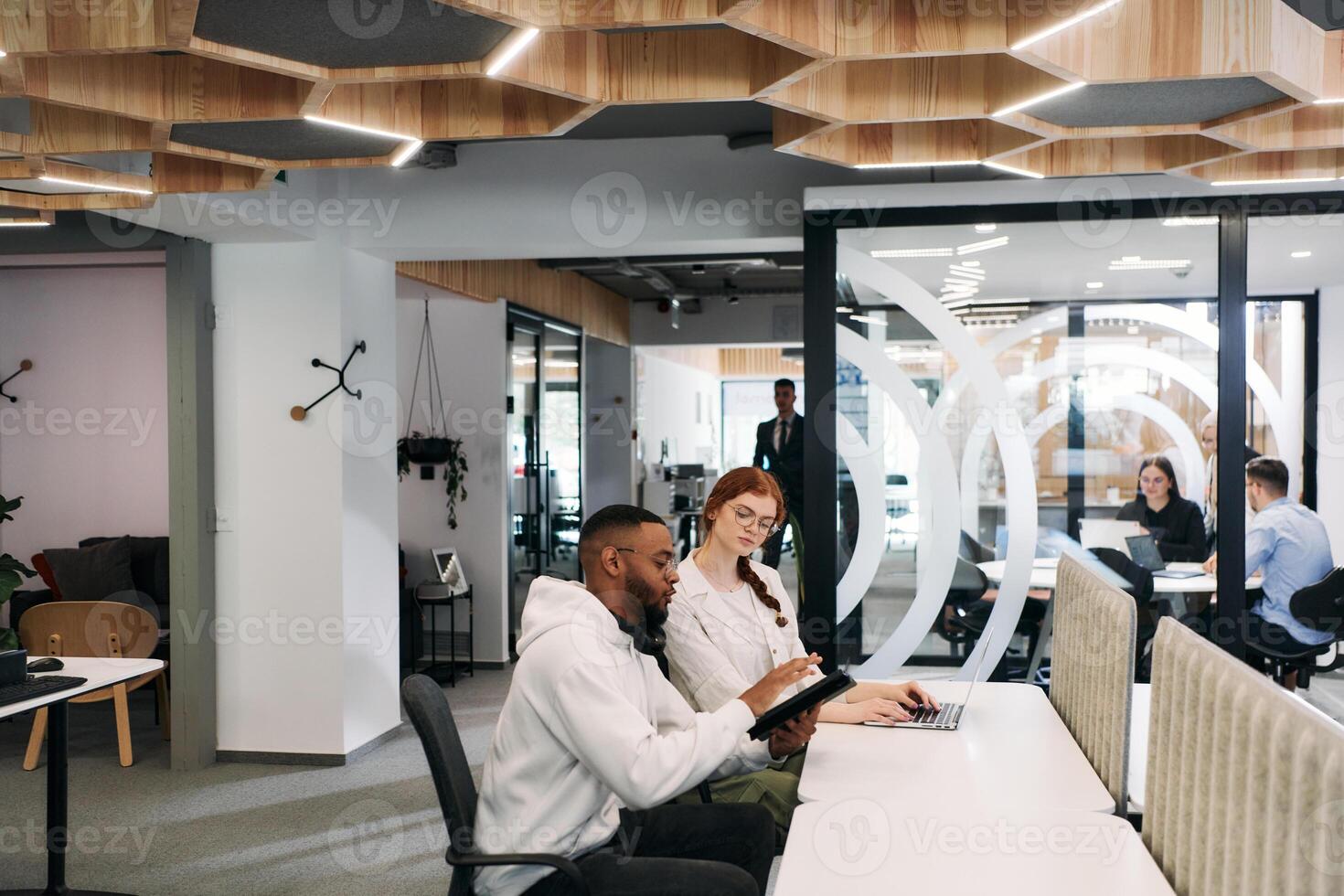 Two colleagues collaborating in a modern office while discussing a project using a tablet and laptop. photo