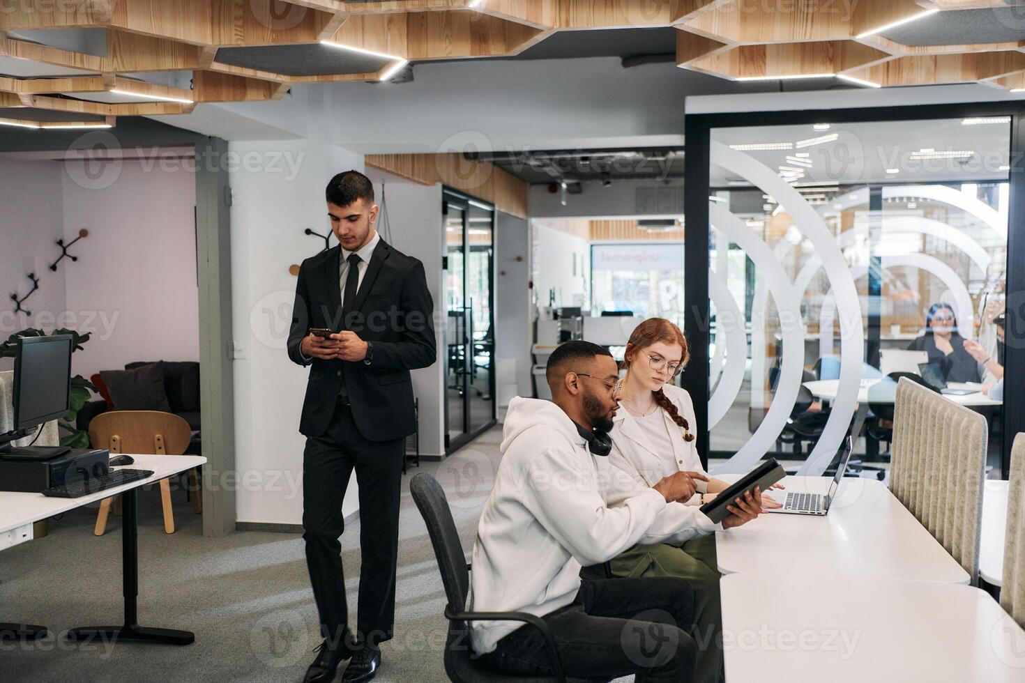 Two colleagues collaborating in a modern office while discussing a project using a tablet and laptop. photo