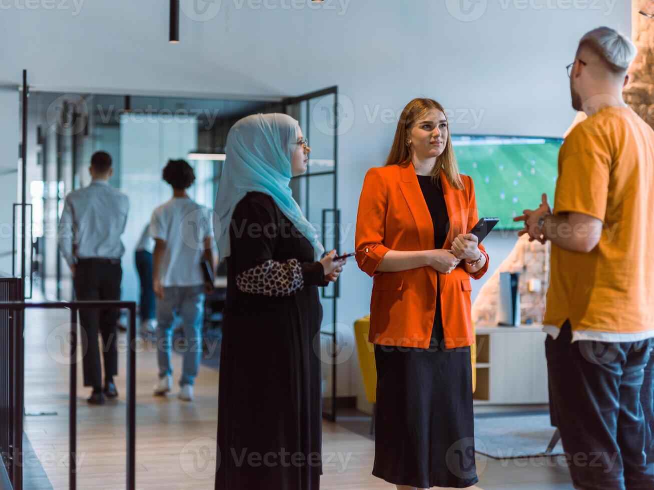 A group of young business colleagues, including a woman in a hijab, stands united in the modern corridor of a spacious startup coworking center, representing diversity and collaborative spirit photo