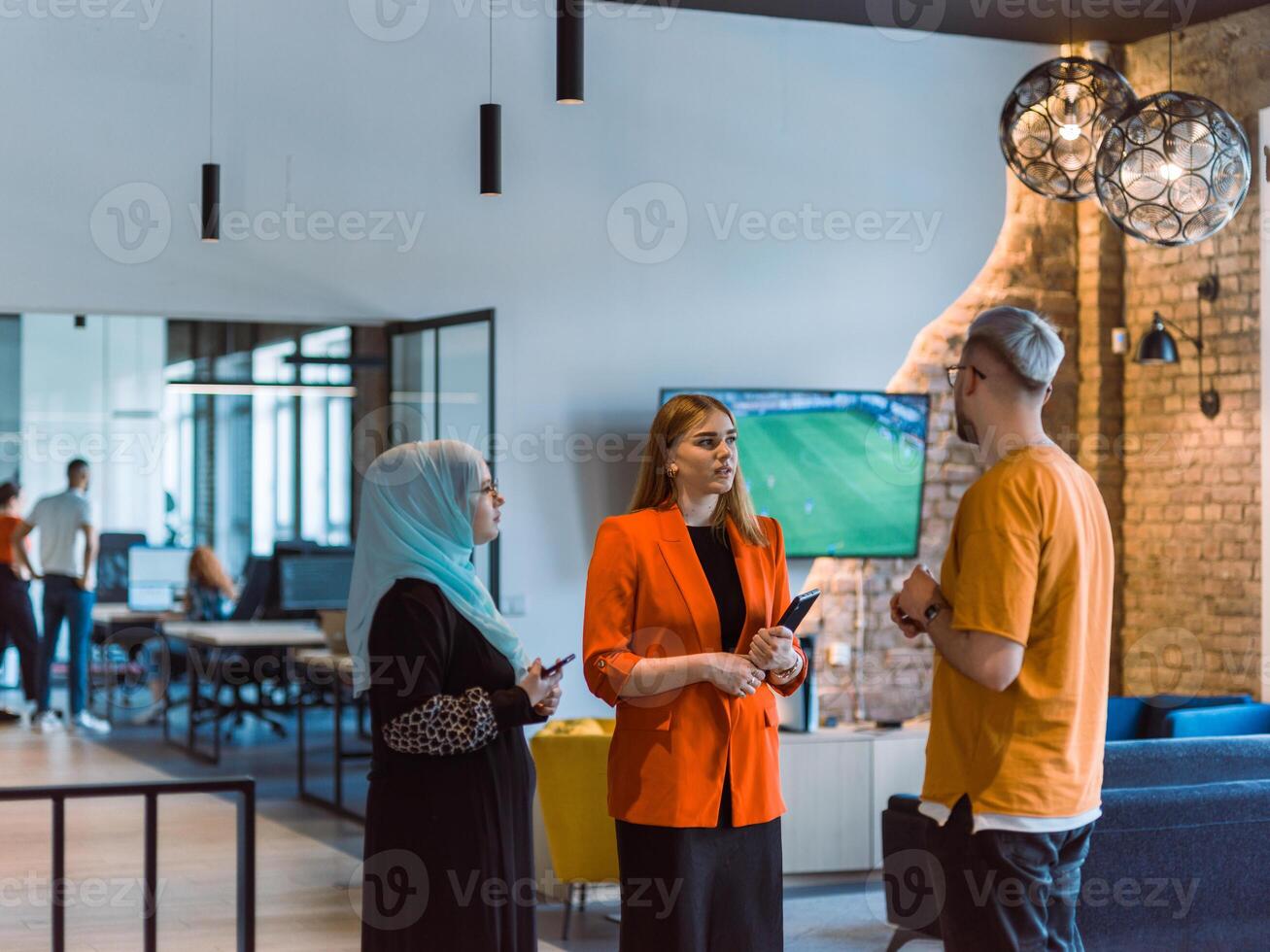 A group of young business colleagues, including a woman in a hijab, stands united in the modern corridor of a spacious startup coworking center, representing diversity and collaborative spirit photo