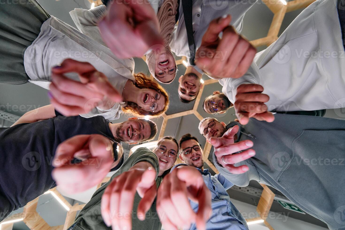 A group of cheerful young people gathered in a circle, pointing at the camera from a low-angle perspective. photo