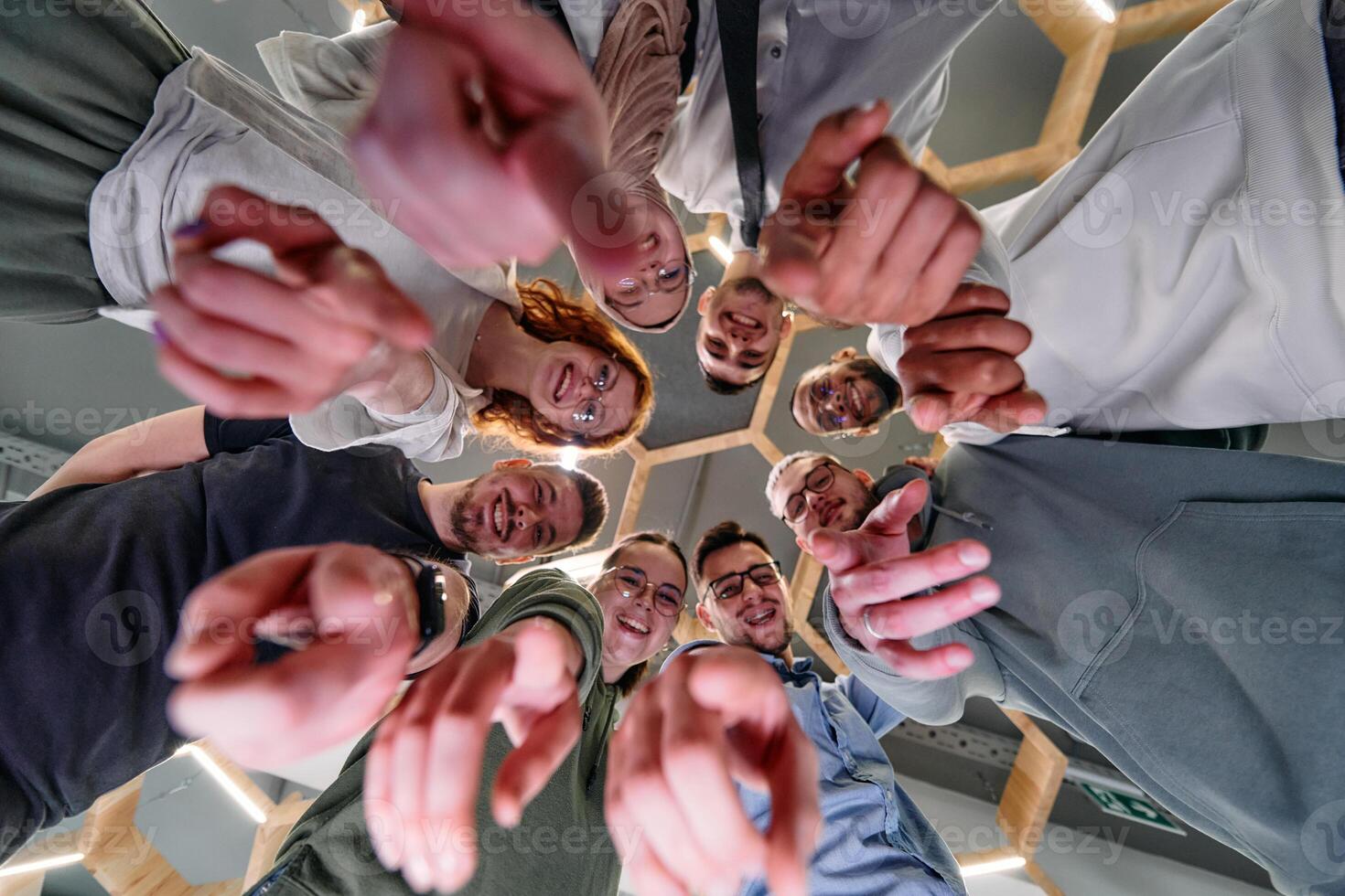 A group of cheerful young people gathered in a circle, pointing at the camera from a low-angle perspective. photo