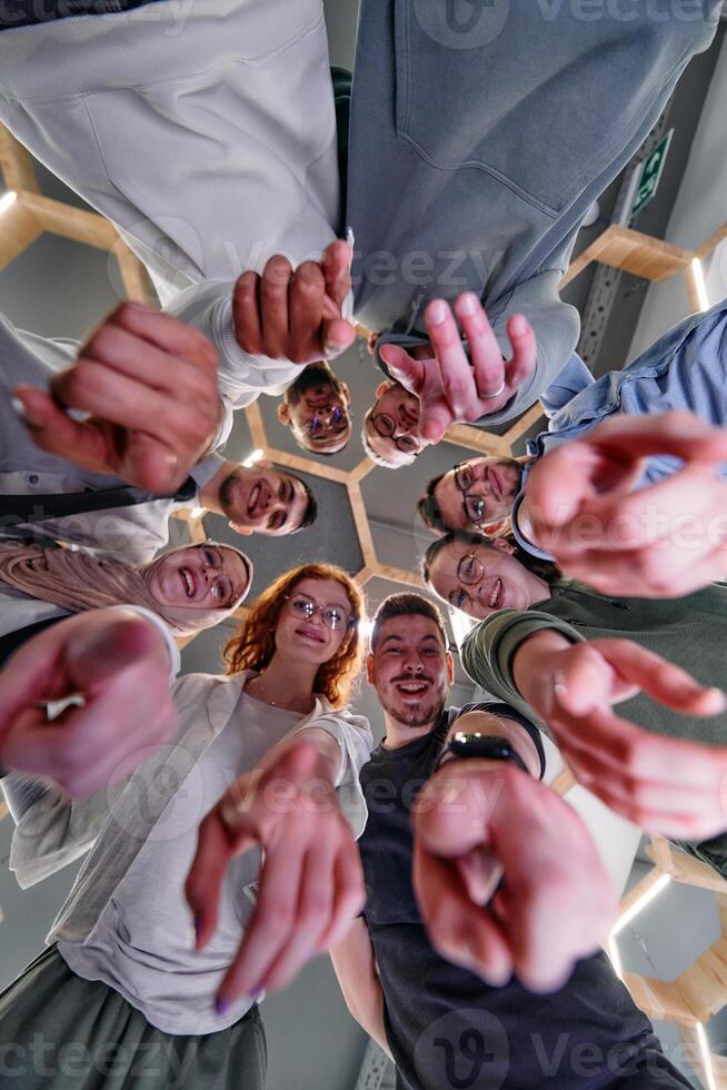 A group of cheerful young people gathered in a circle, pointing at the camera from a low-angle perspective. photo