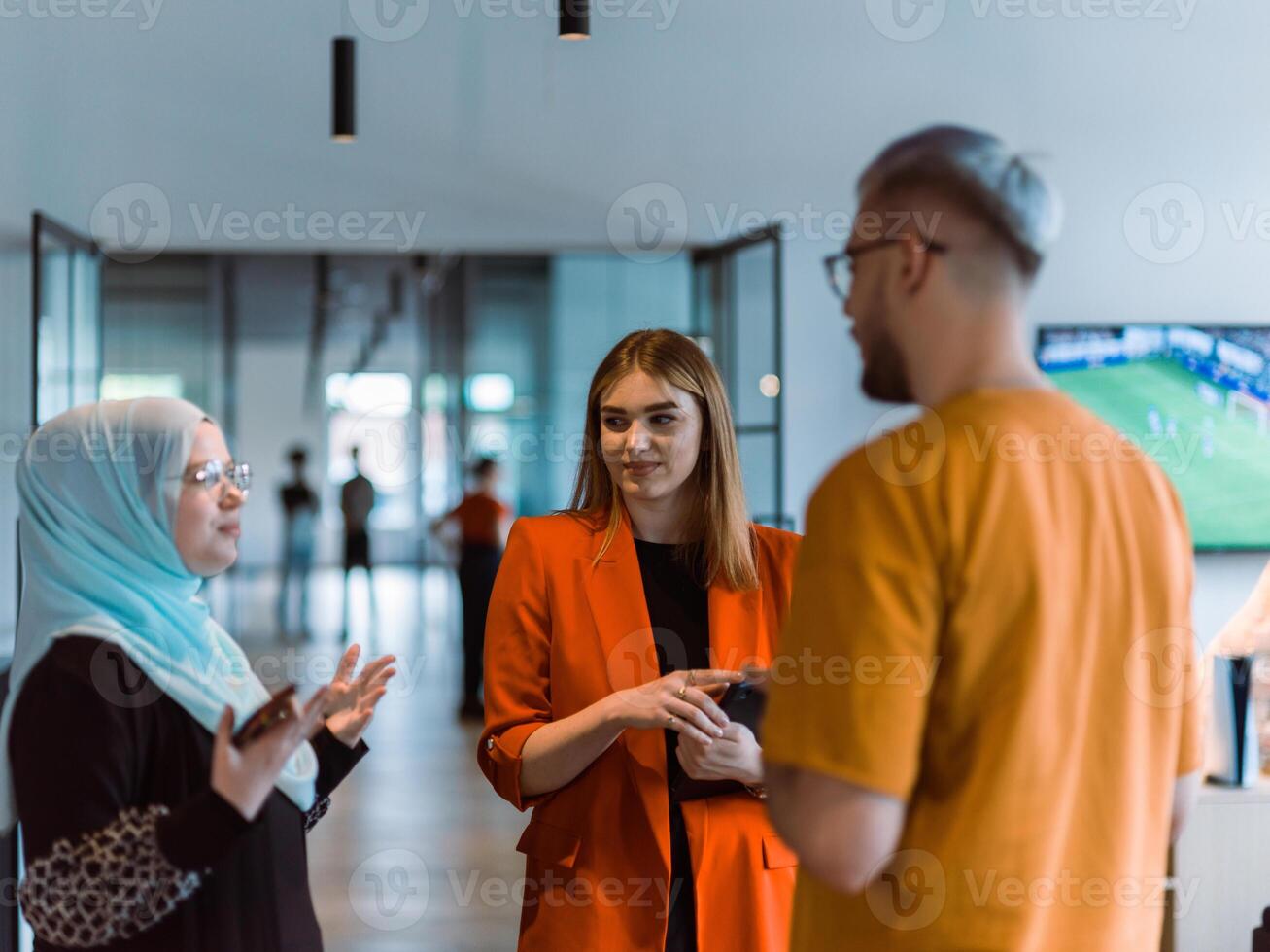 A group of young business colleagues, including a woman in a hijab, stands united in the modern corridor of a spacious startup coworking center, representing diversity and collaborative spirit photo
