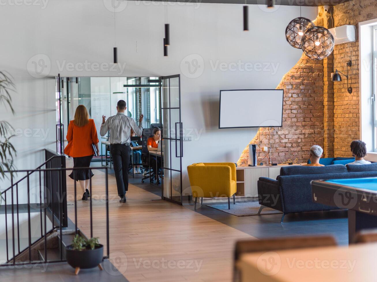 A business group, including an African American businessman in a wheelchair, collaborates within a modern glass office, actively engaged around a computer and laptop, collectively solving diverse photo