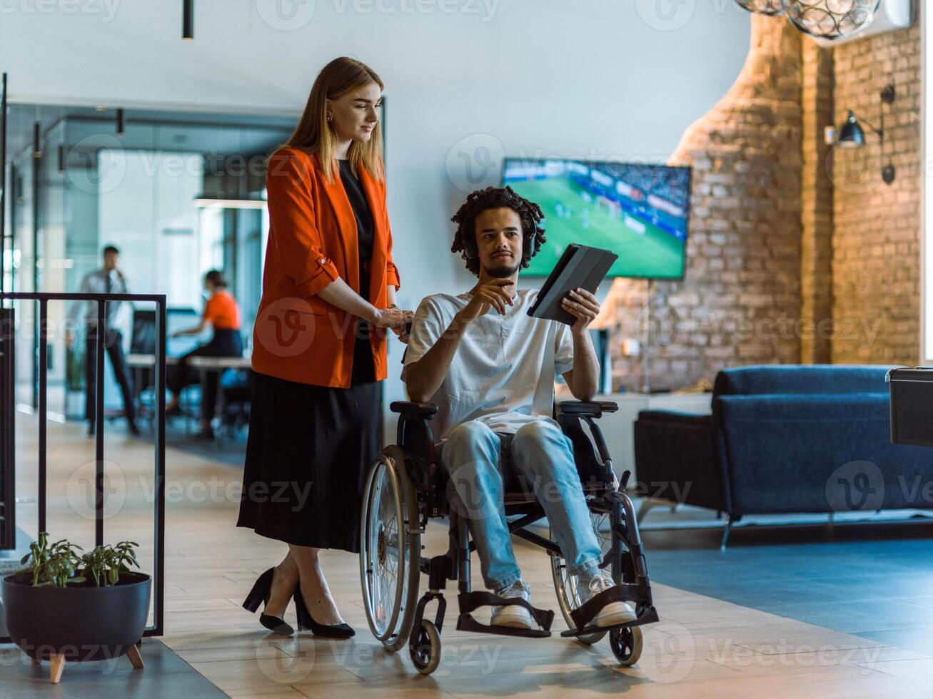 African-American businessman in a wheelchair engages in a collaborative discussion, using a tablet, with his business colleague, exemplifying the seamless integration of adaptive technology and photo