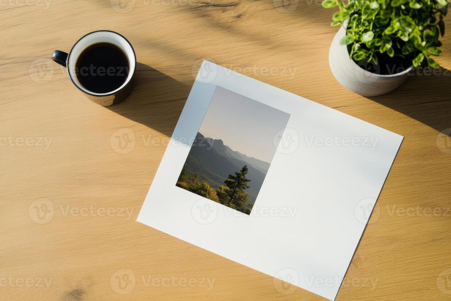 Coffee and a landscape print on a wooden table with a green plant in the background during a calm morning photo