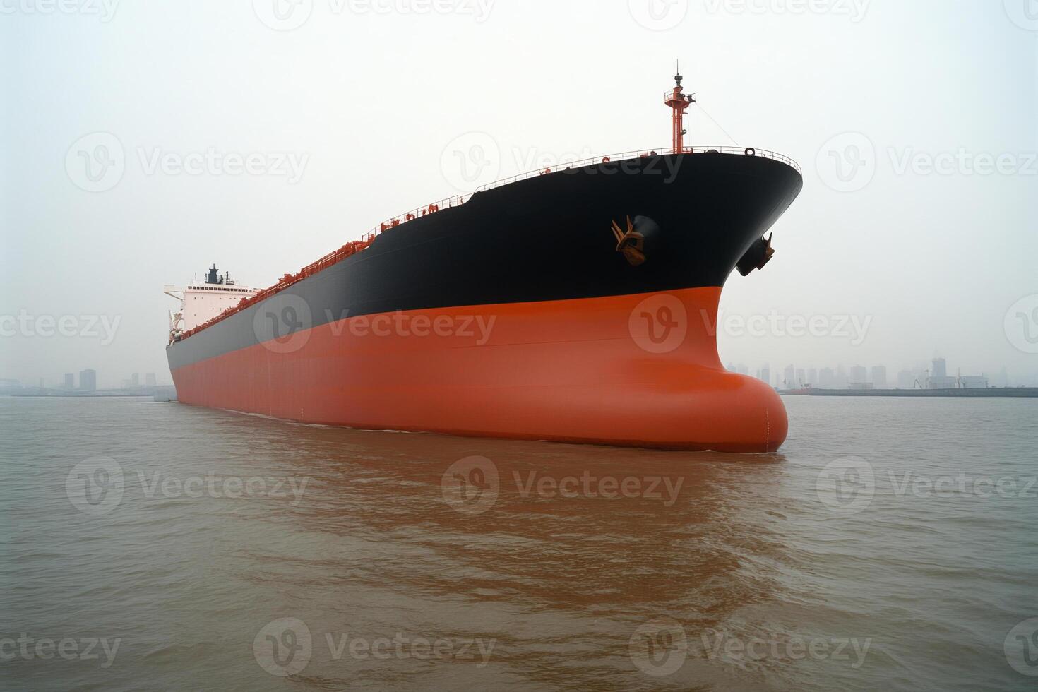 Large cargo ship navigating through foggy waters near a city coastline in the early morning hours photo