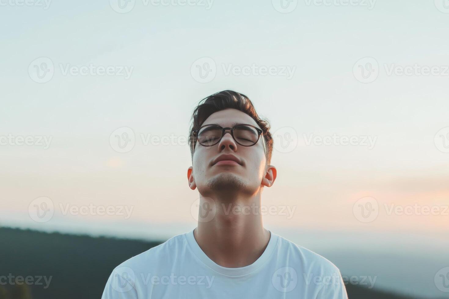 Young man enjoys serene moment outdoors at sunset while wearing glasses, embracing tranquility in nature photo