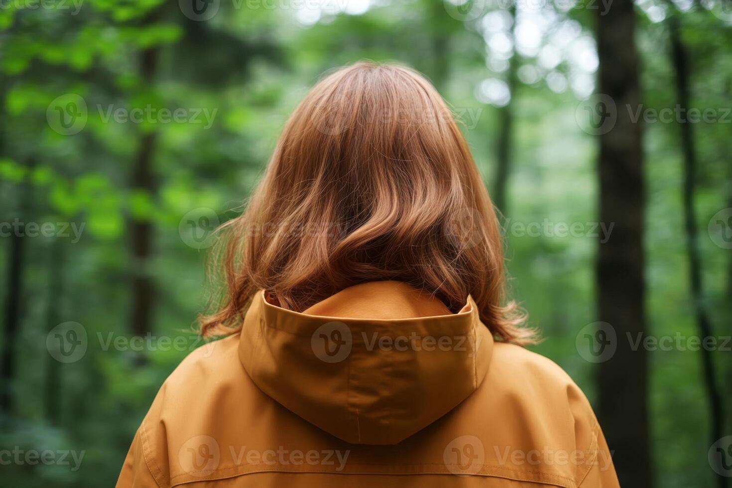 Person in a brown jacket stands in a lush green forest surrounded by tall trees and vibrant foliage on a calm day photo