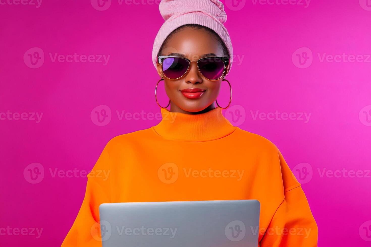 A fashion-forward woman wearing a vibrant orange sweater and pink headscarf types on a laptop, displaying confidence and style. photo