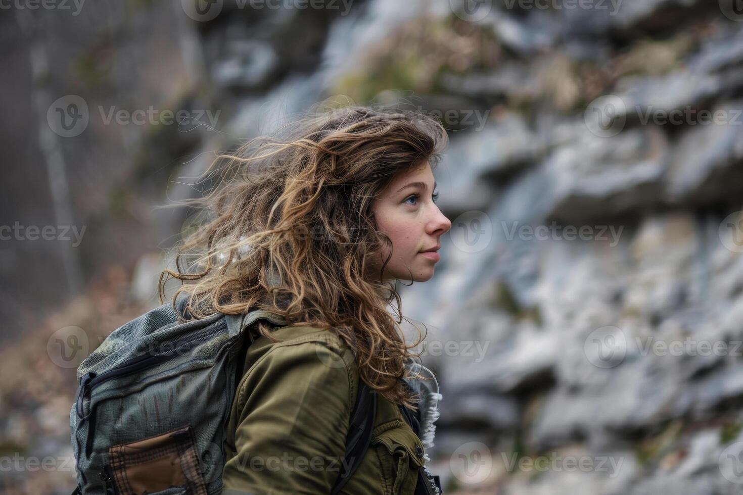 A woman with a backpack standing in front of a rock wall photo
