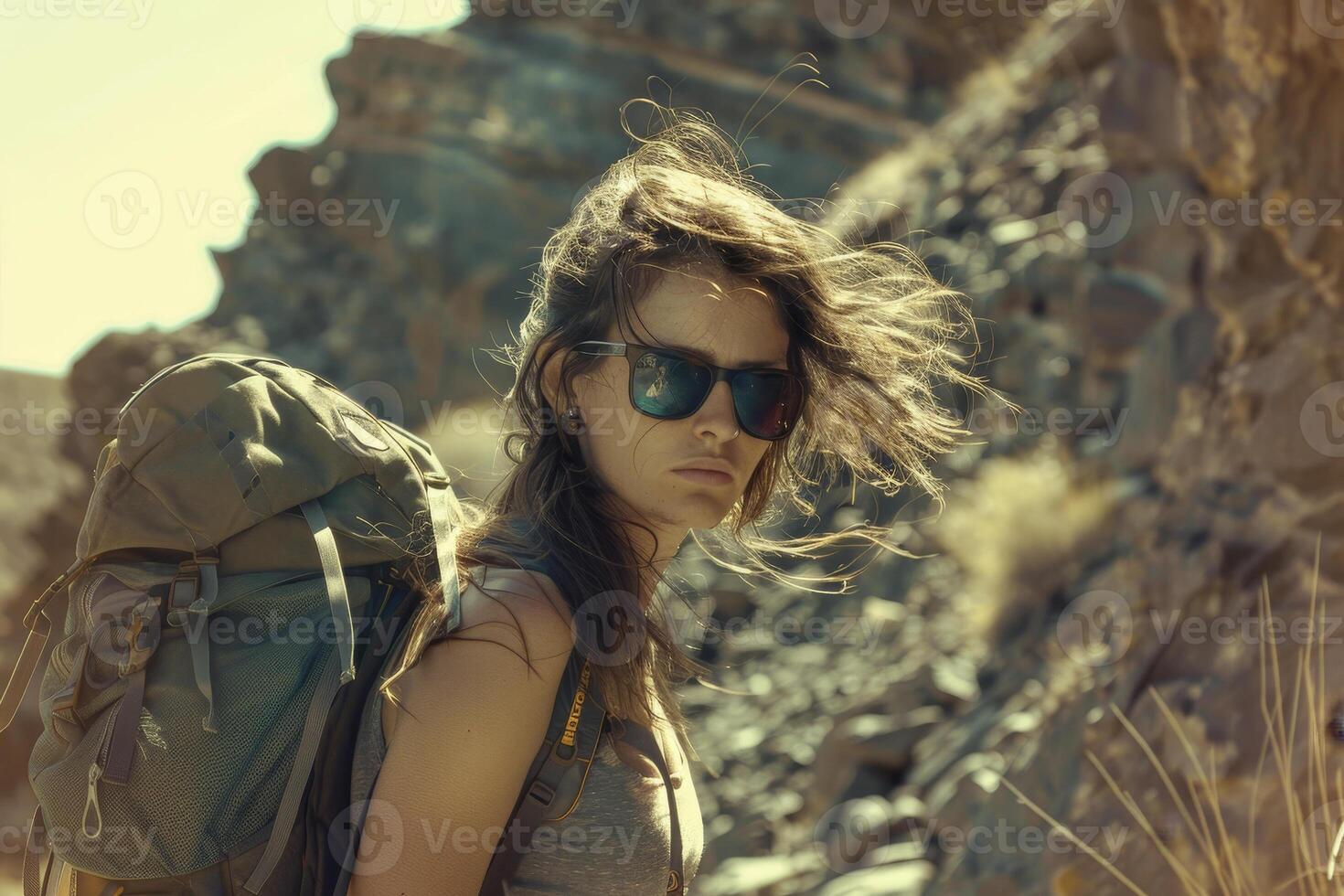 A woman with a backpack and sunglasses standing in the desert photo