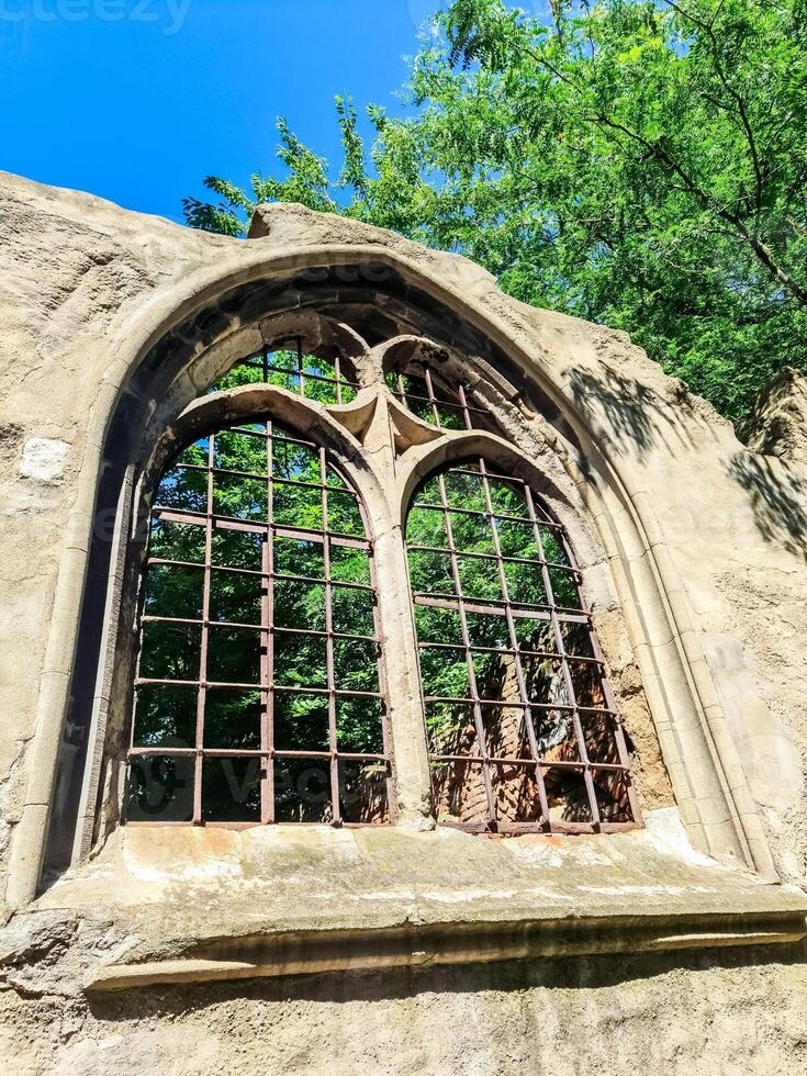 Old ruined arched window showing lush green tree and blue sky photo
