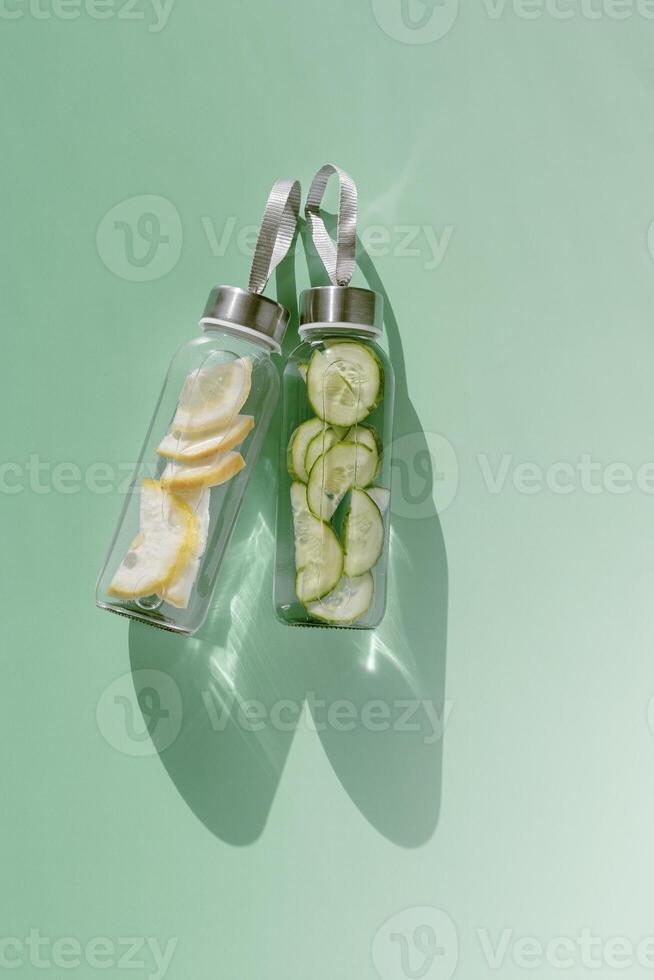 Glass bottles with lemon, cucumber water drink detox at sunlight on green colored background, copy space. Healthy infused water boost metabolism, weight loss. Aesthetic still life, refreshing drink photo
