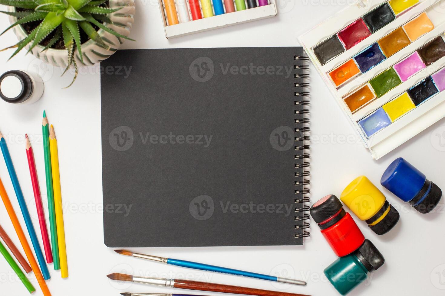 Black sketchbook on a white table with drawing supplies. photo
