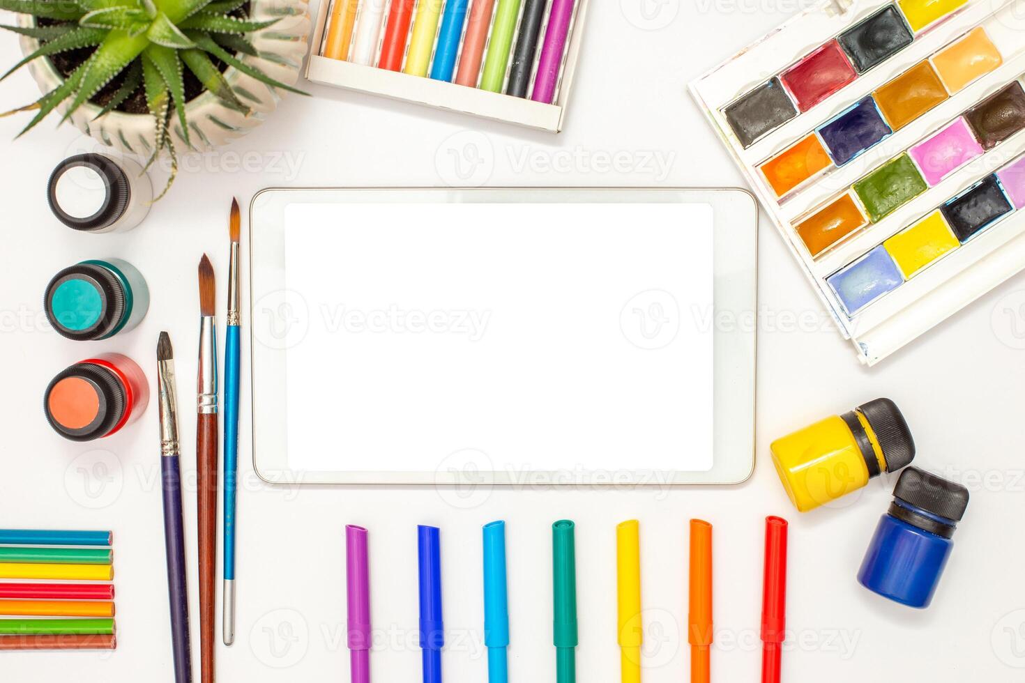 White digital tablet with a blank screen on table and drawing supplies photo