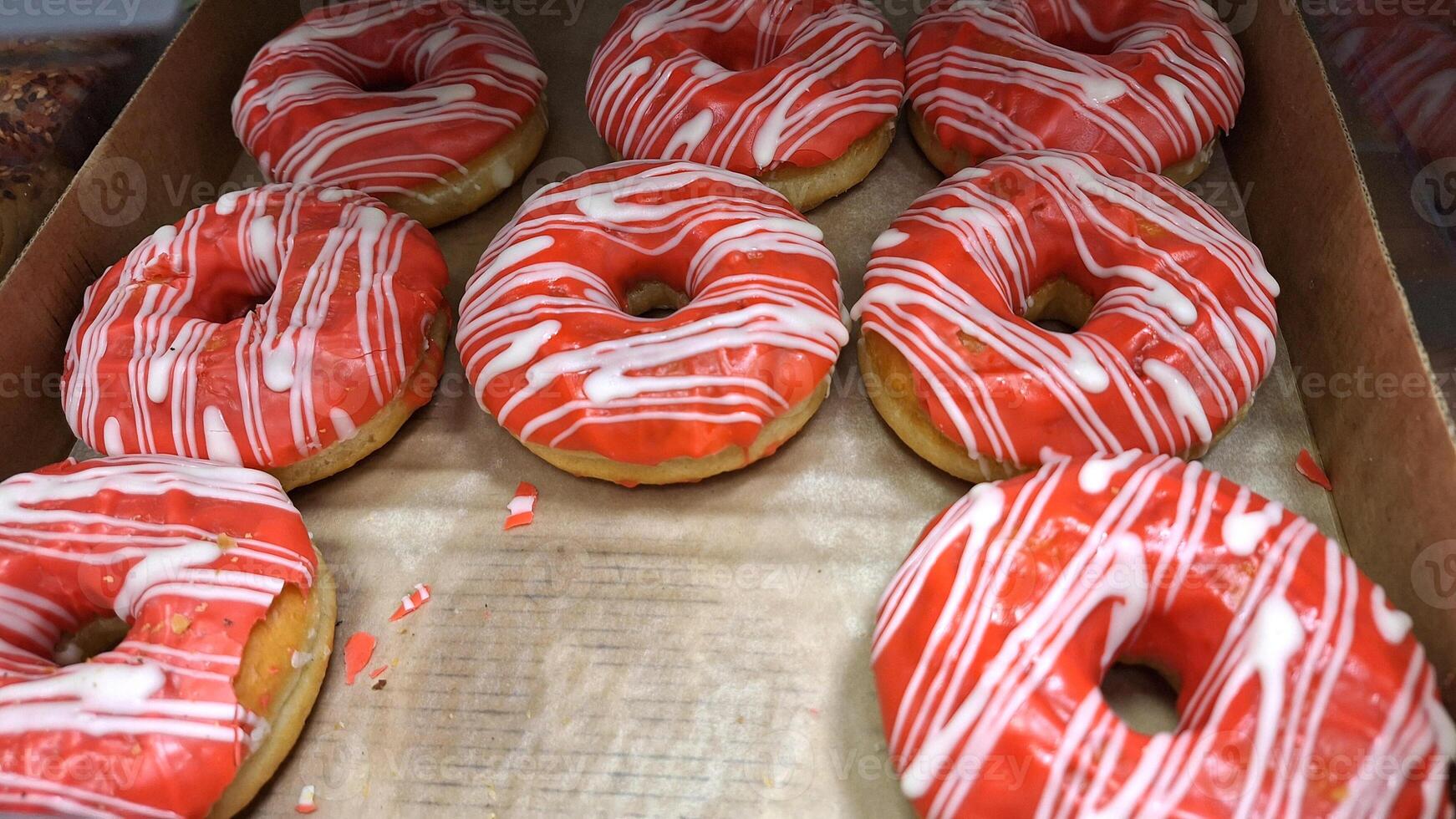 Vibrant red iced donuts with white drizzle arrangement in cardboard box photo