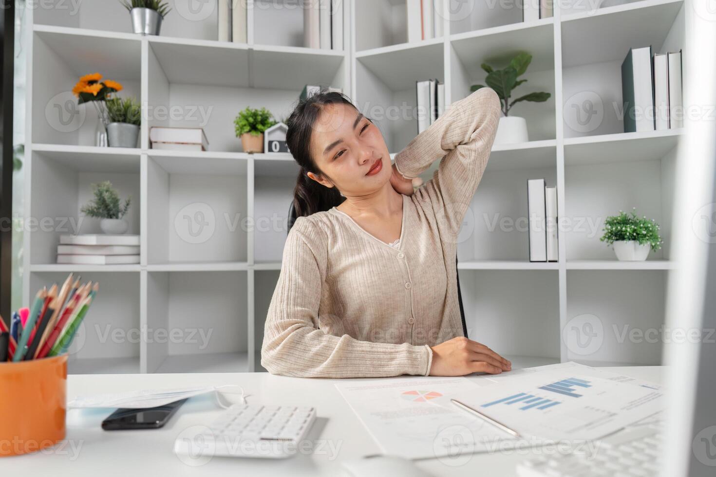 Woman stretching neck while sitting at her desk, experiencing office syndrome symptoms. photo