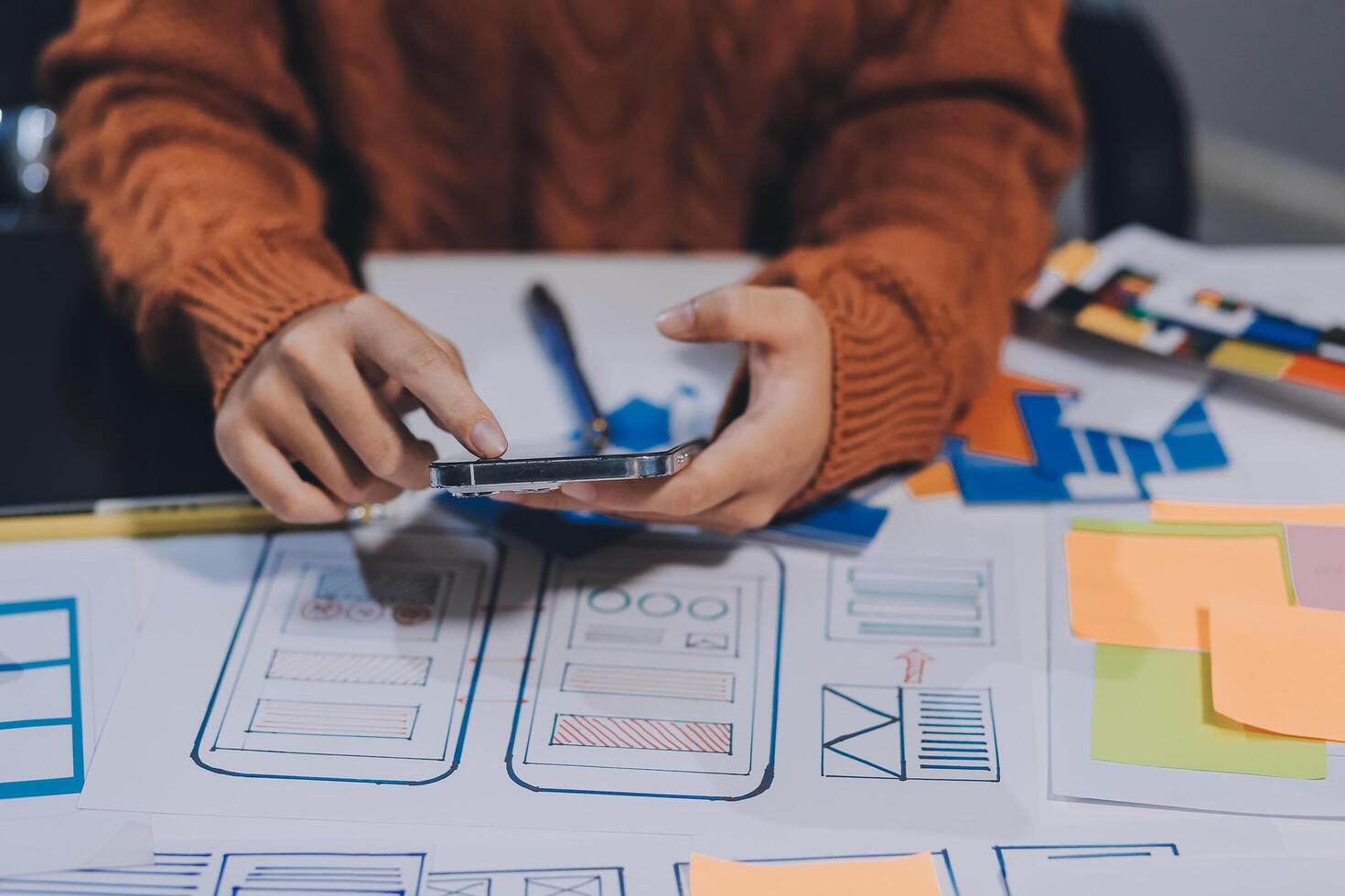 A person is using a cell phone while sitting at a desk with a bunch of paper and other photo