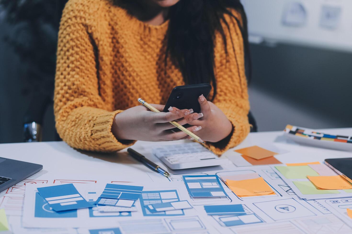 A woman is using her phone while sitting at a desk with a laptop and a notebook photo