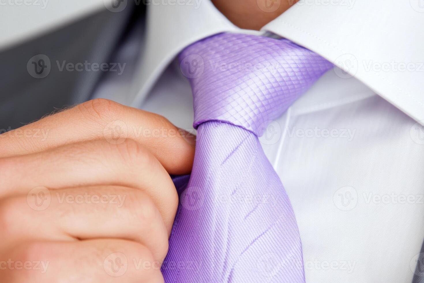Close-up of a man adjusting a lilac tie with a white dress shirt, emphasizing luxury and elegance in soft lighting photo