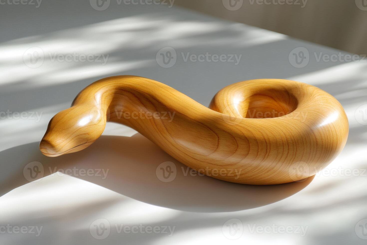 Wooden snake sculpture illuminated by sunlight resting on white surface photo