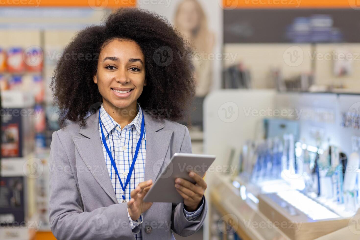 A smiling retail employee standing in an electronics store, holding a tablet. The professional is dressed in a blazer and name tag, ready to assist customers with their tech purchases. photo