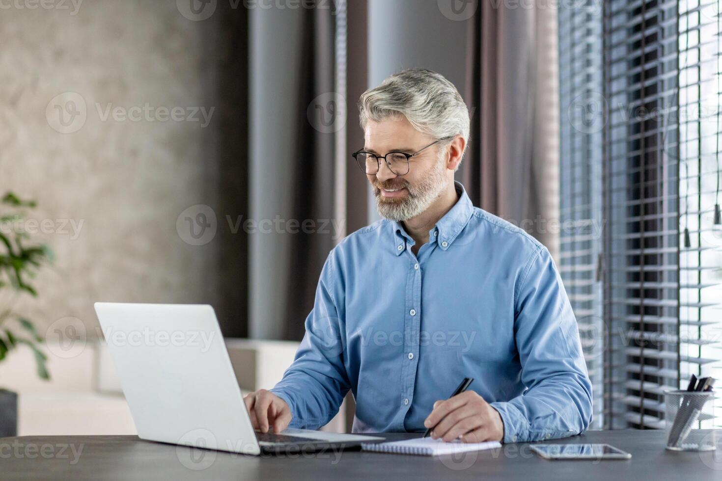 Smiling businessman working on laptop at office desk in a modern, professional setting. Concept of professional, modern office environment, and productivity. photo