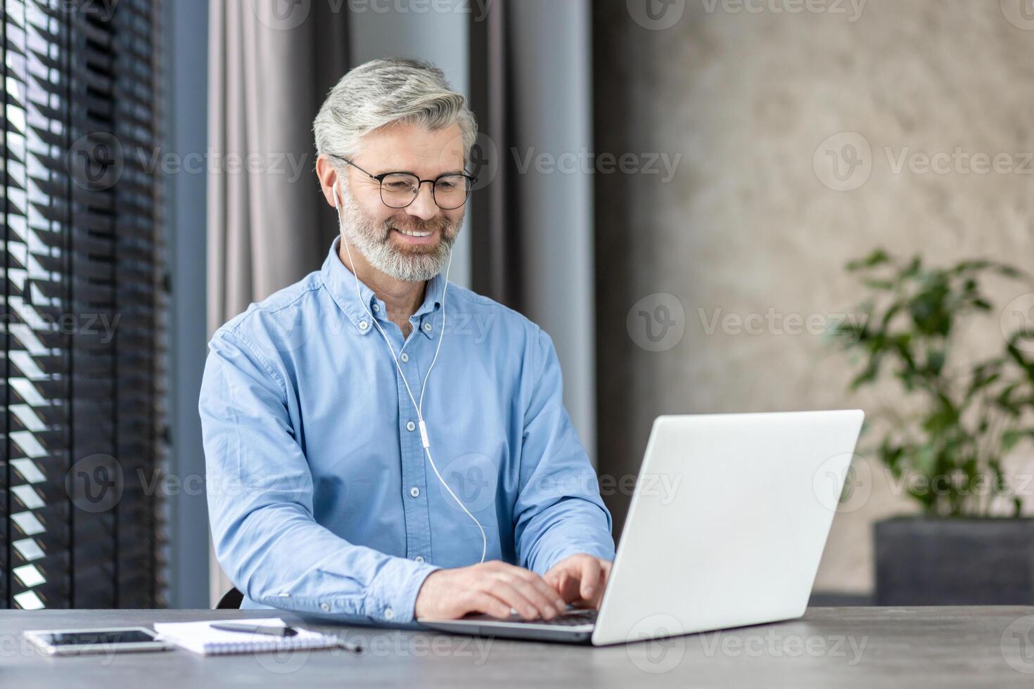 Smiling mature businessman using a laptop for remote work or online communication. Professional working from home or office setting. photo