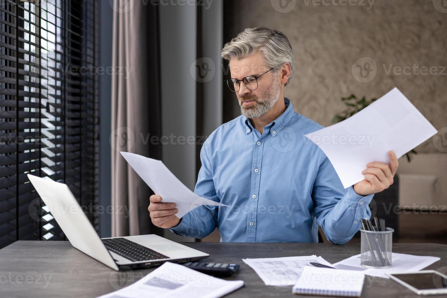 Middle-aged businessman analyzing papers at his office desk. Professional working on important tasks with concentration. photo