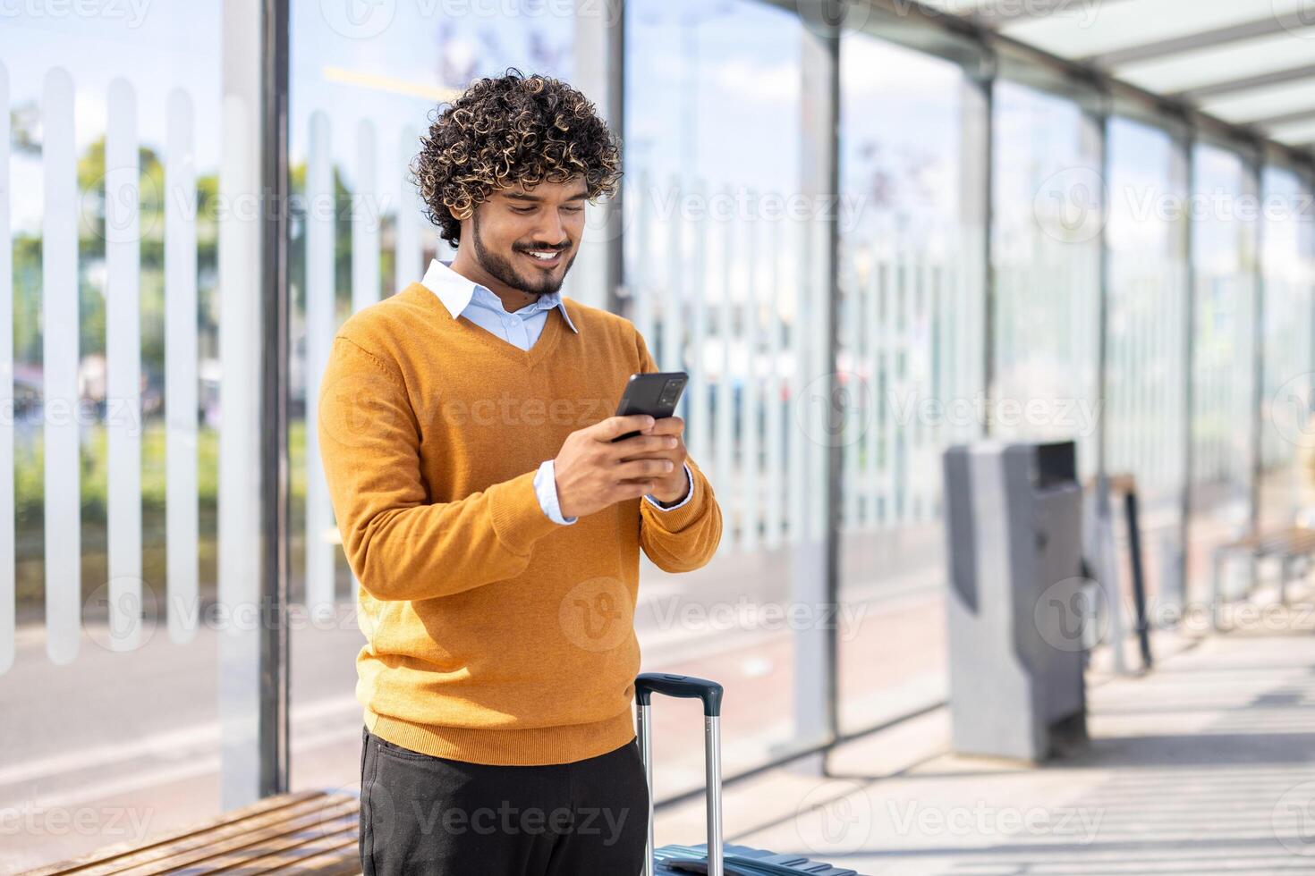 Man holding phone while standing at public transport stop. Passenger buys tickets remotely online, smiling happily, waiting for bus or tram. photo