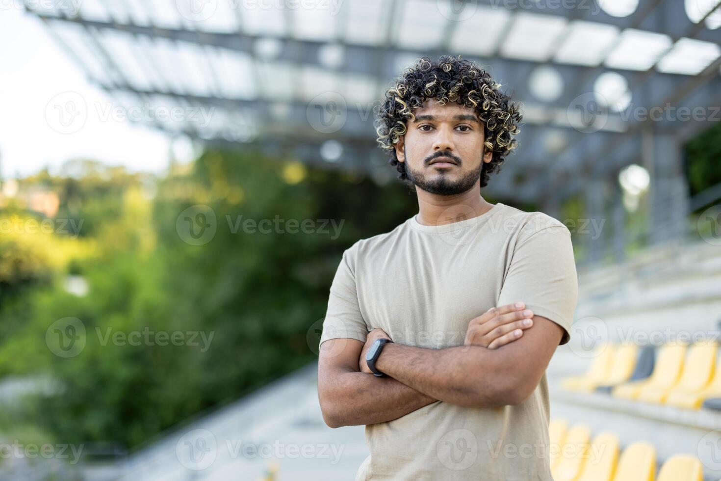 Portrait of serious confident man in sportswear at stadium. Athlete calmly looking at camera with crossed arms. photo