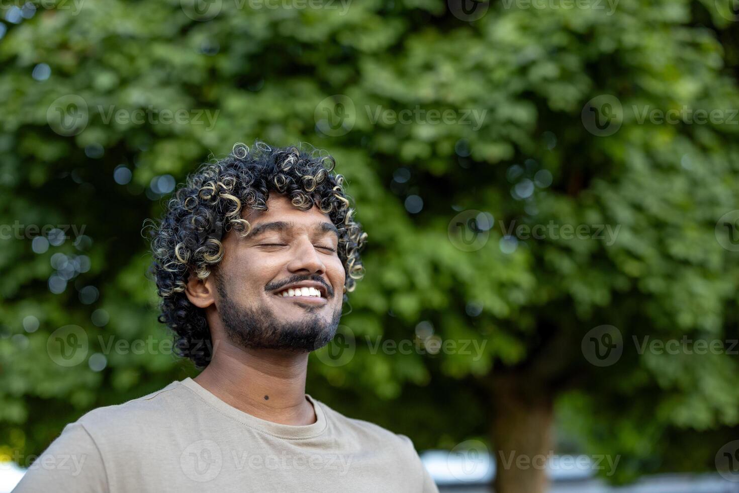 Close-up of a man resting, relaxing and doing breathing exercises, smiling contentedly with his eyes closed, walking in a park among the trees. photo