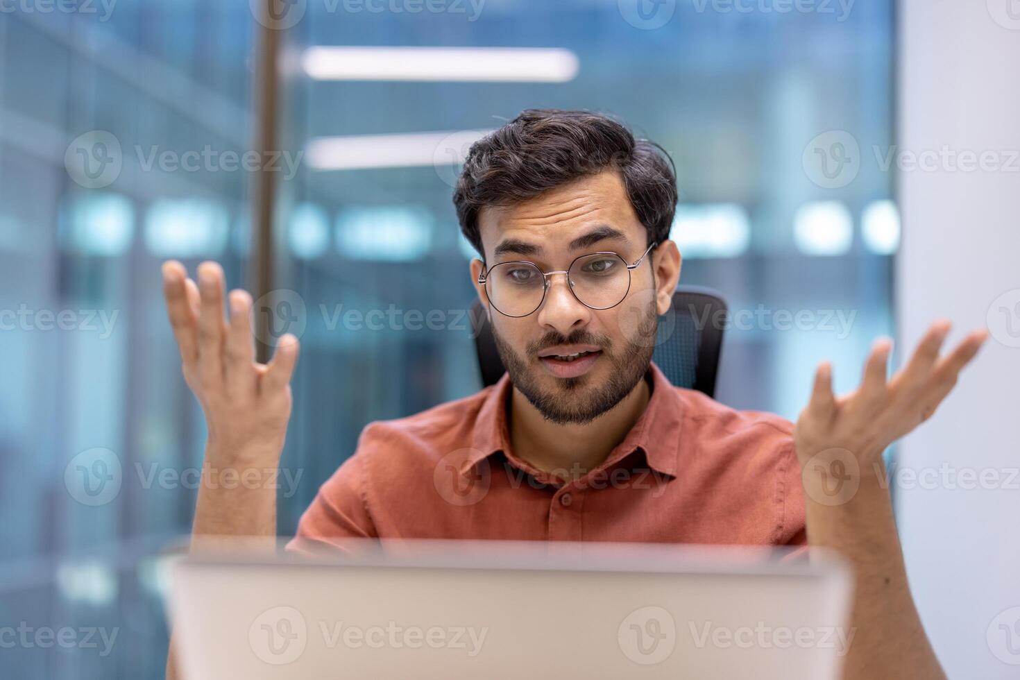 Young professional in casual shirt engaging in online call, expressing enthusiasm and curiosity. Conceptualizes communication and workplace dynamics in modern business environment. photo