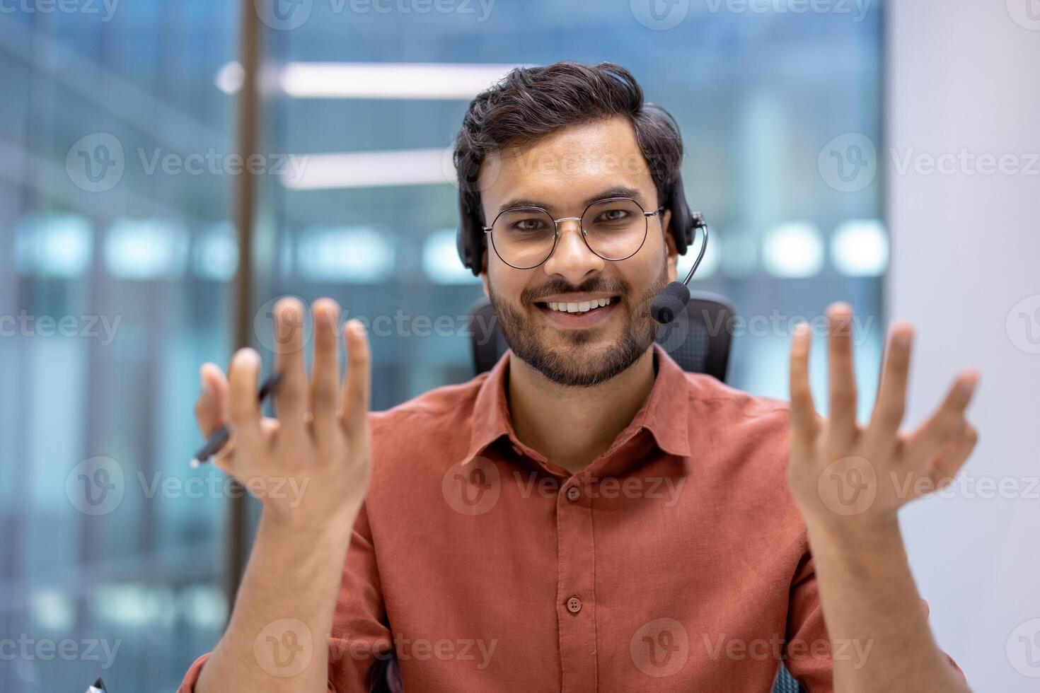 Latin American man businessman smiling during online call wearing headset in office. Engaging interaction with open-hand gestures creates warm, welcoming atmosphere. photo