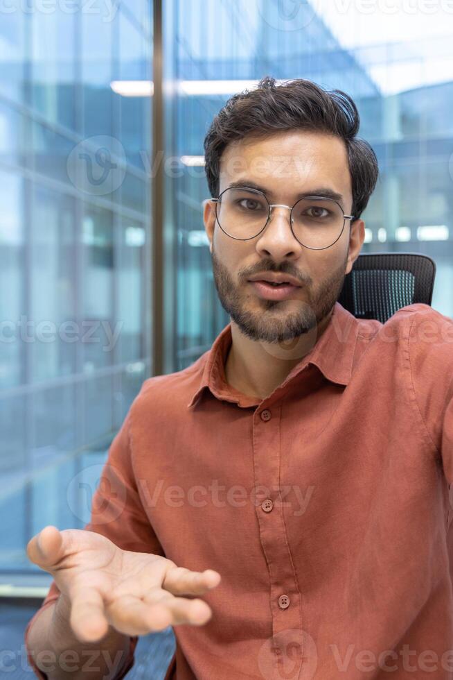 Businessman wearing glasses engaged in call gesturing with hand in modern office. Professional communication and interaction through phone. Confident expression, focused conversation photo