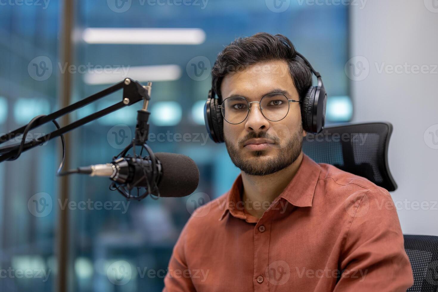 Serious male broadcaster with glasses and headphones sits in studio recording podcast. Professional setting conveys focus and expertise. Capturing essence of modern media and communication. photo