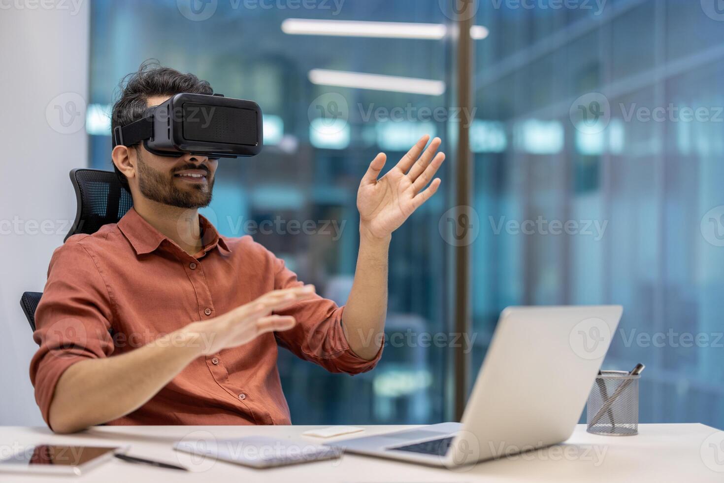 Man using VR headset immersed in virtual reality seated at office desk. Hands engaged in interaction with digital content. Modern workplace environment showcasing technology innovation and engagement photo